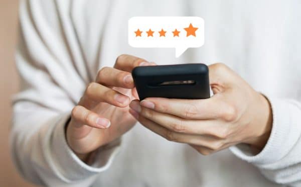 close up on customer man hand pressing on smartphone screen with gold five star rating feedback icon