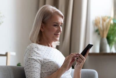 Older woman looks at her phone while browsing on her couch